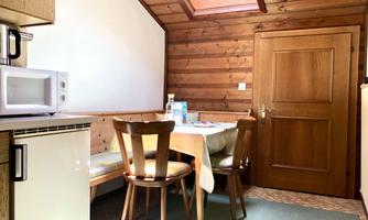 A cozy kitchen with wooden walls and a dining area. There is a table with chairs and various kitchen appliances.
