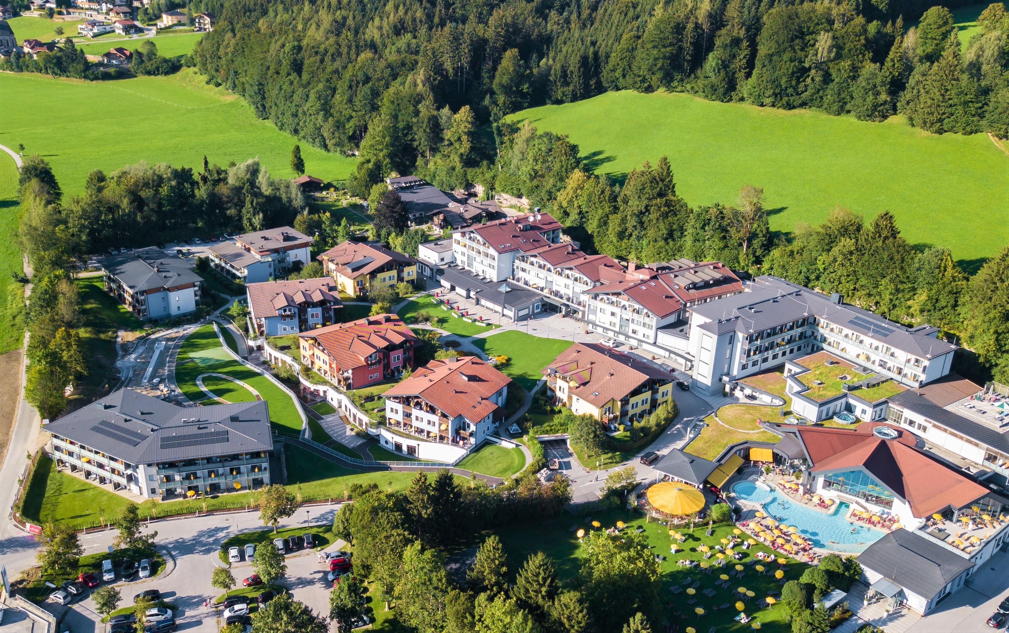 A picturesque hotel complex surrounded by green meadows and trees. In the foreground, various buildings and recreational facilities can be seen.