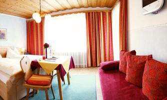 A cozy hotel room with a double bed and a small table. Red curtains and a couch create an inviting atmosphere.