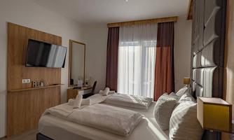 A modern hotel room with two beds and large windows. There is a television, a desk, and stylish furniture.