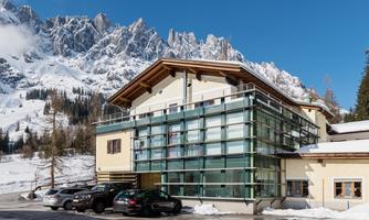 A modern building in the mountains, surrounded by snow-covered landscapes. Clear blue sky and majestic peaks in the background.