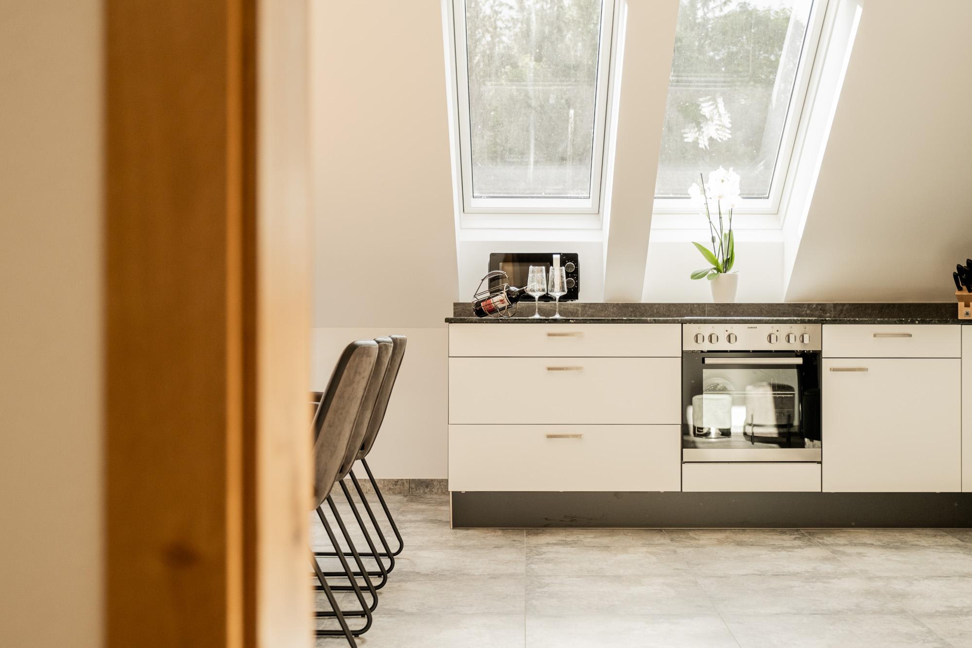 A modern kitchen with sloping ceilings and plenty of daylight. The gray floor and elegant furnishings create an inviting atmosphere.