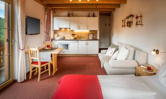 A cozy living space with a small kitchenette and a dining table. The decor is bright and inviting, featuring a red bedspread.