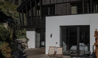 A modern house with wooden elements and large windows. On the terrace, there are two loungers and a round hot tub.