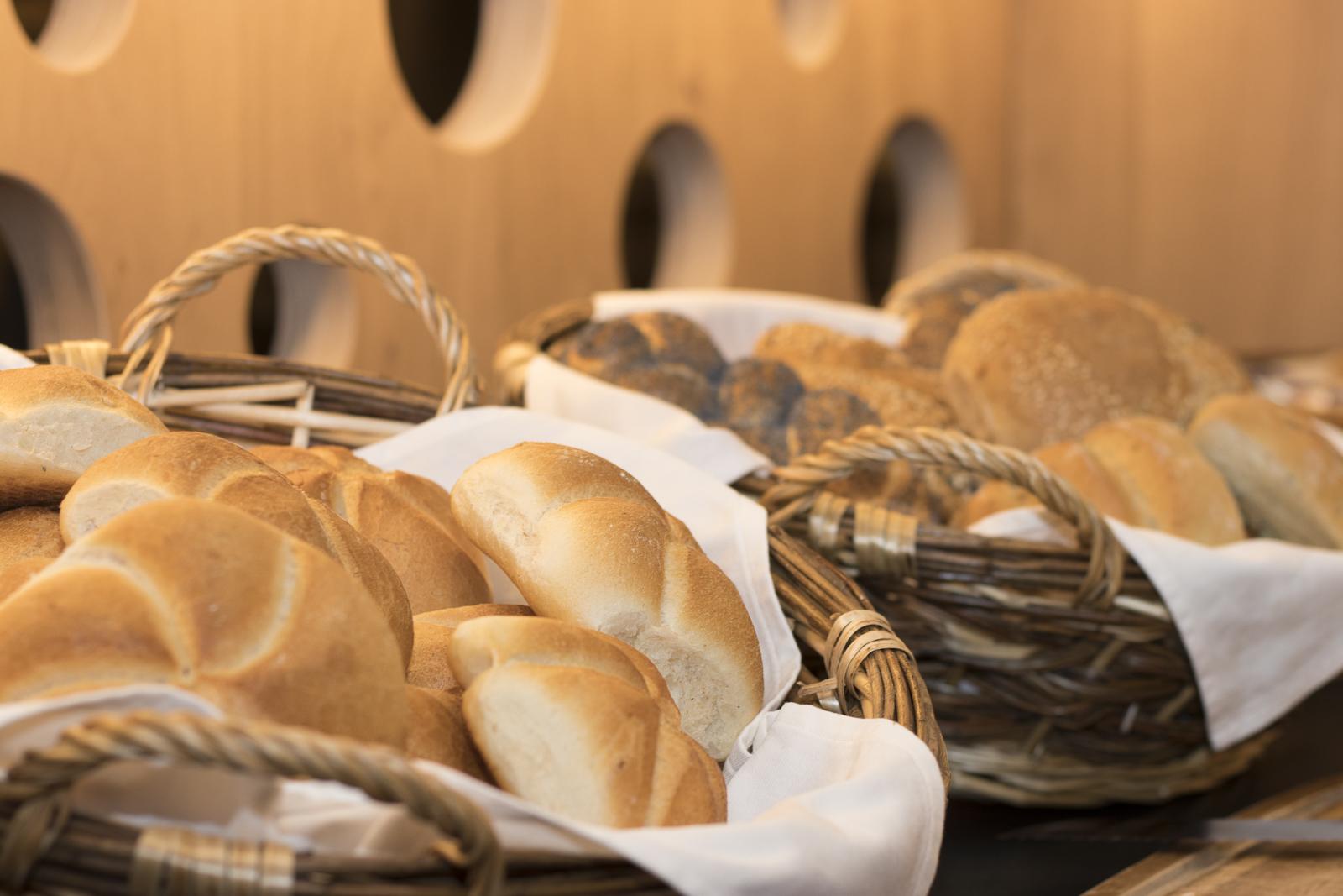 A basket with fresh rolls and brownish pastries. The breads are beautifully arranged and invite you to enjoy.