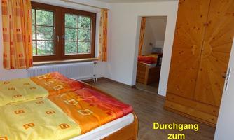 A cozy bedroom with a double bed and a wooden wardrobe. A passage leads to the children's room.