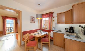 A cozy kitchen with wooden cabinets and a dining table. This seats four people and has large windows overlooking the outside.