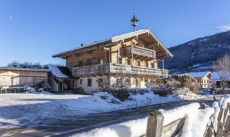 A charming wooden house in the mountains, surrounded by snow-covered landscapes. The bright blue sky complements the wintry atmosphere.