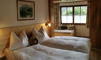 A cozy bedroom with two beds and wooden decor. Large windows provide plenty of daylight and a welcoming atmosphere.