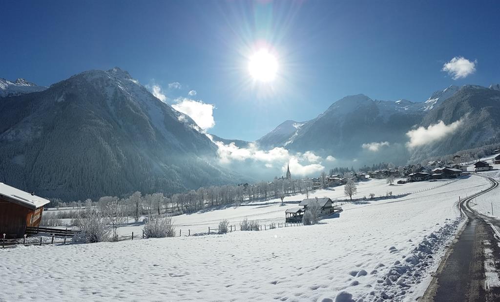A picturesque winter landscape with snow-covered mountains and a clear sky. The sun shines brightly over a calm, snowy scenery.