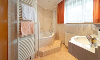 A modern bathroom with a bathtub and a shower. The walls are brightly tiled, and large windows let in plenty of light.