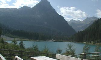 A quiet lake surrounded by mountains and forest. A wooden bench and a table invite you to linger.