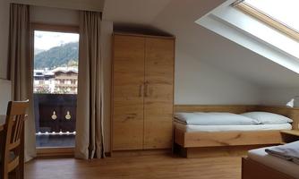 A cozy bedroom with wooden furniture and a window that offers a view of the mountains. The room has a warm atmosphere and bright lighting.