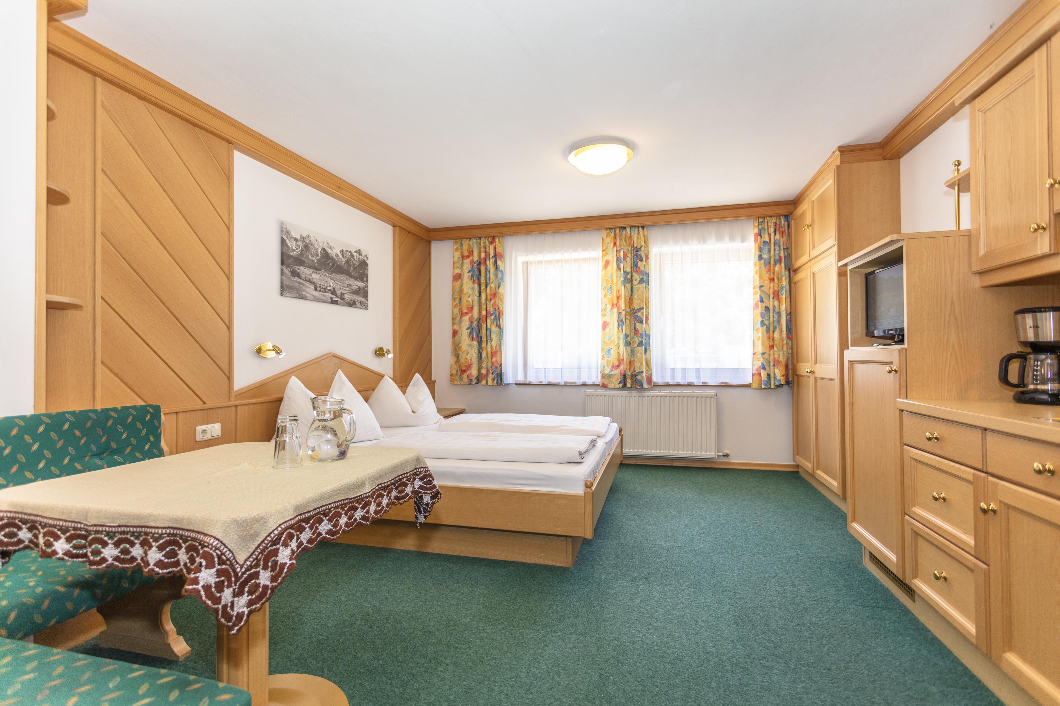 A cozy room with two single beds, a seating area, and a table. The walls are bright and decorated with colorful curtains.