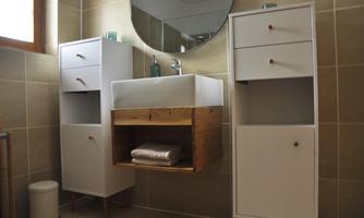 A modern bathroom with bright tiled flooring. The furniture is in white and wood, with a round mirror above the sink.