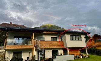 A modern house with a green garden and a balcony. The holiday apartment is clearly marked.