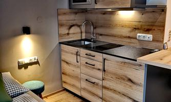 A modern kitchen with wooden surfaces and a modern stove. The room is bright and inviting, with a small sofa in the corner.