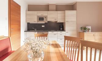 A modern kitchen with wooden fronts and a cozy dining area. A vase with flowers is on the table.