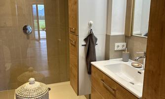 A modern bathroom with wooden cabinets and a spacious shower. There is a rug on the floor and a laundry basket stands next to the sink.
