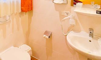 A small bathroom with a toilet, a sink, and a towel holder. The walls are light, and there is a large window curtain in bright orange.