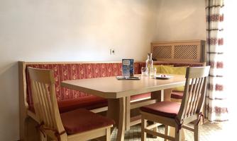 An inviting dining area with a wooden table and four chairs. The walls are light, and there is a cozy bench with red cushions.