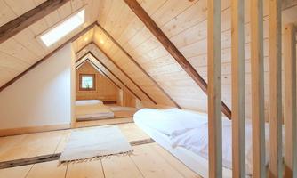 A cozy attic with wooden ceilings and two beds. Natural light streams through the window, creating an inviting atmosphere.