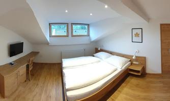 A modern bedroom with two single beds and a wooden wardrobe. The room has large windows and a friendly, bright atmosphere.