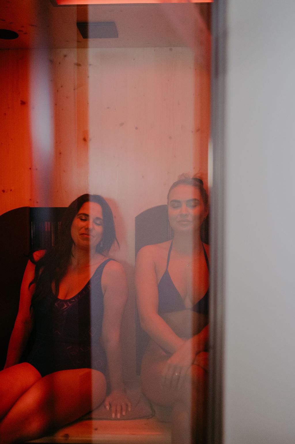 Two women are relaxing in a sauna with red light. The atmosphere is warm and soothing.