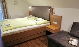 A cozy room with a double bed and an adjacent sofa. The walls are bright and the decor is simple, with a lovely view of daylight.