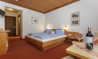 A cozy hotel room with two beds and soft pillows. On the table, there is a bottle of wine and two glasses.