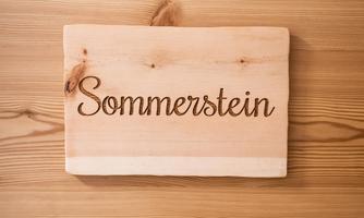 A wooden sign with the inscription "Sommerstein". The lettering is elegant and easily readable on the light wood surface.