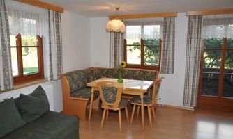 A cozy dining area with a U-shaped seating corner and a dining table. Large windows let in plenty of light and offer a view of nature.