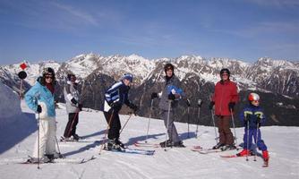 A group of skiers stands on a snow-covered slope in the mountains. The landscape is impressive with snow-capped peaks in the background.