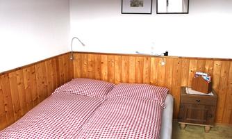 A cozy bedroom with a double bed and checkered bedspreads. On the wall, there are wooden paneling and two picture frames.