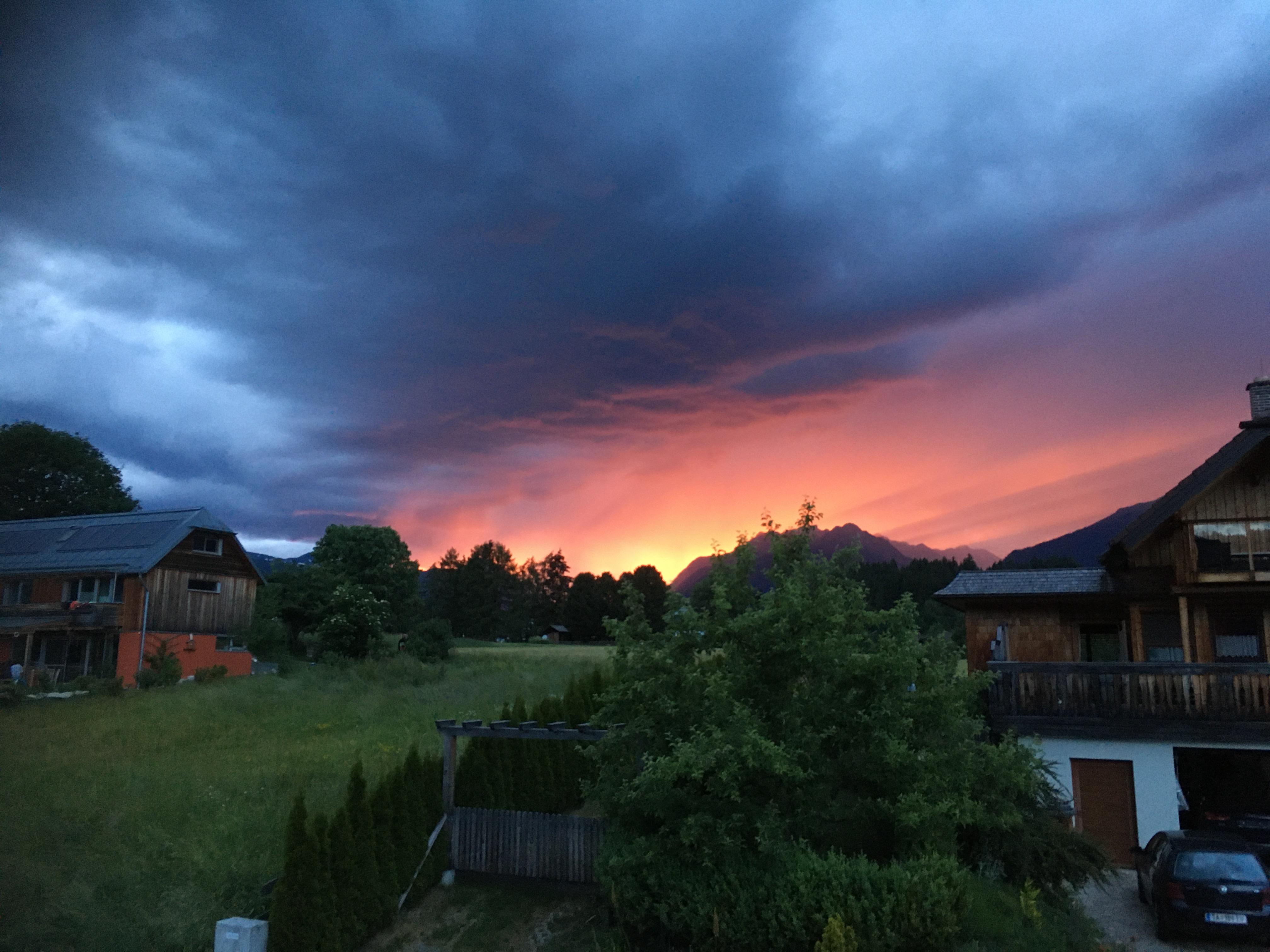 An impressive sunset behind dark clouds over a tranquil village. The colors shine in orange and pink and are reflected in the landscape.