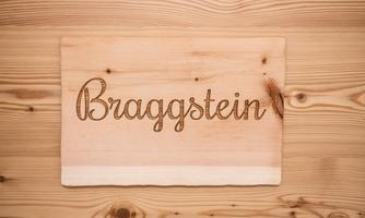 A wooden sign with the inscription "Braggstein". The background consists of a light wood surface.