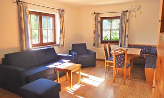 A bright living room with blue sofas and a wooden table. Large windows provide plenty of daylight.