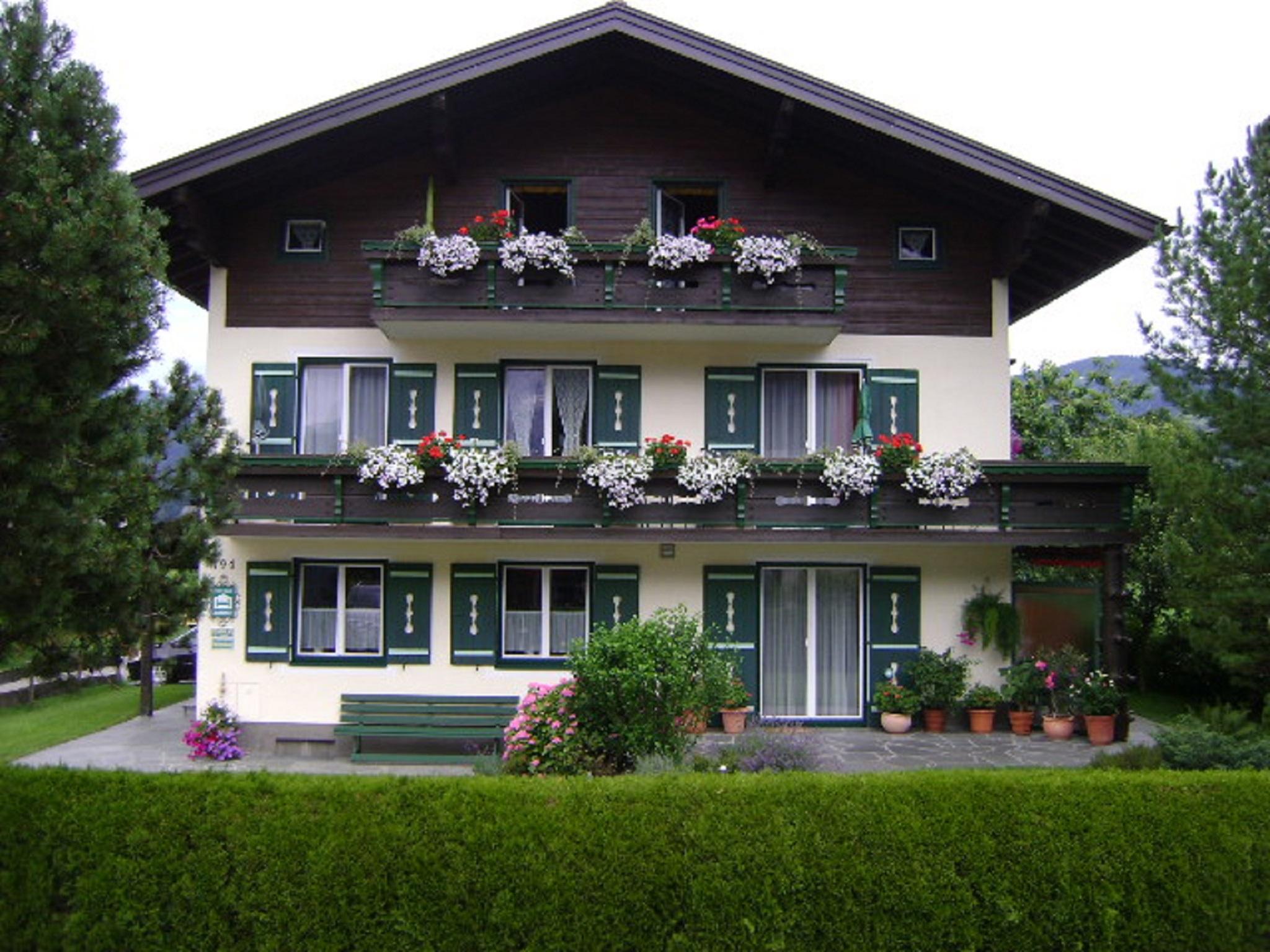 A charming house with flower balconies and green shutters. Surrounded by a well-maintained garden and trees.