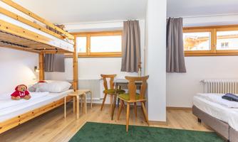 A cozy sleeping room with a bunk bed and a single bed. The room has large windows, a small table, and a carpet.
