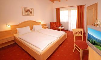 A cozy bedroom with a double bed and warm colors. A television and a small seating area complement the decor.