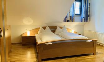 A cozy bedroom with a double bed and white pillows. The wooden floors and gentle colors create an inviting atmosphere.