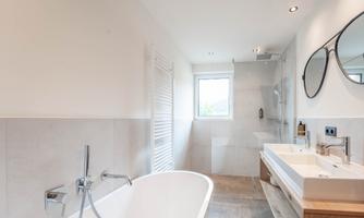 A modern bathroom with a freestanding bathtub and two sinks. Bright walls and natural light sources create an inviting atmosphere.