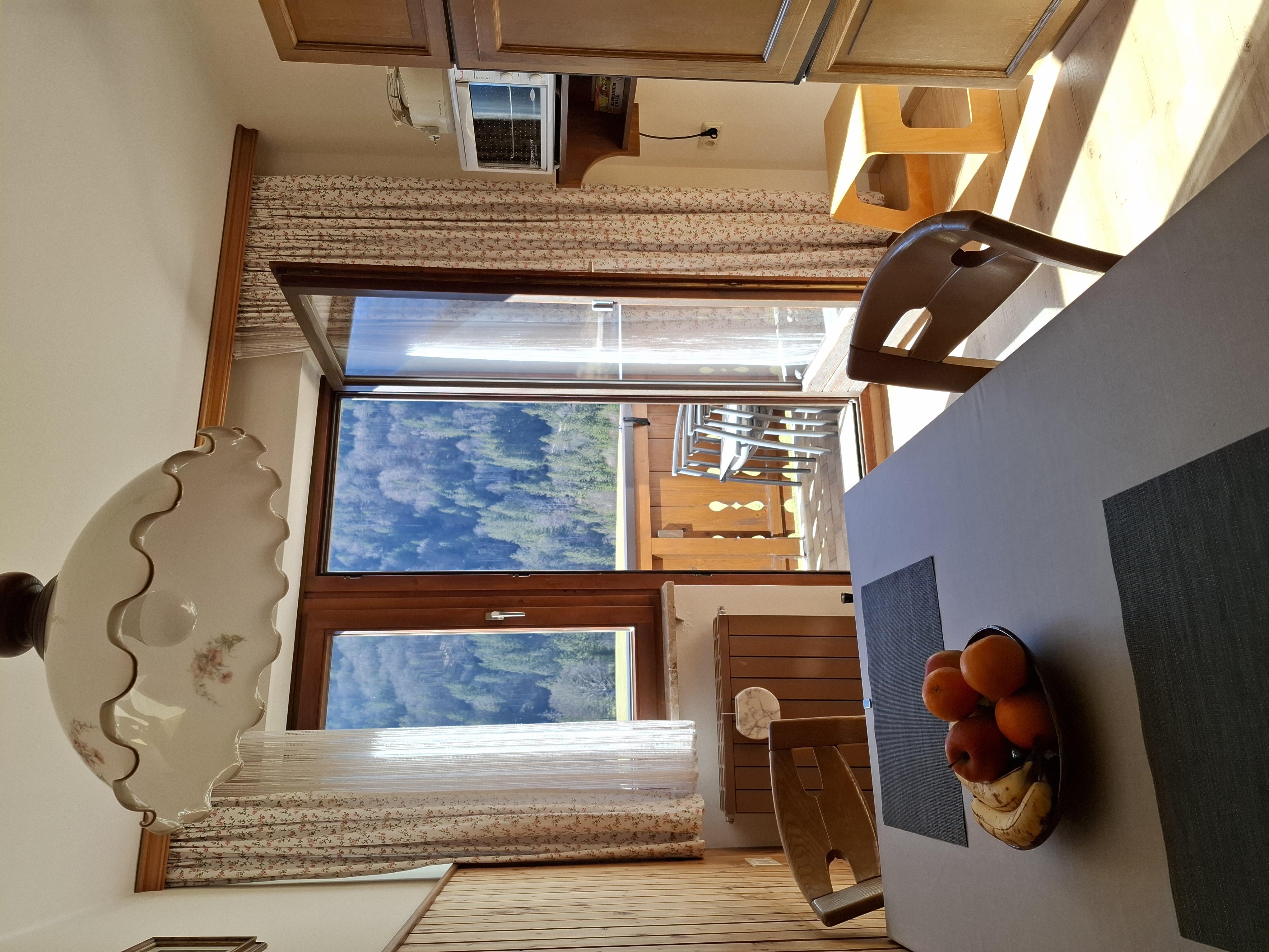A cozy dining table with fruit bowls and a large window that overlooks a mountain view. The room is bright and invitingly designed.