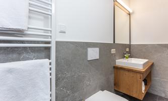 A modern bathroom with a wooden washbasin and a mirror. White towels hang on a towel warmer on the wall.