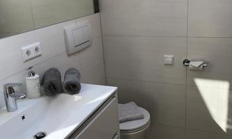 A modern bathroom with a bright tiled floor and an elegant sink. There are towels and a large skylight that provides daylight.