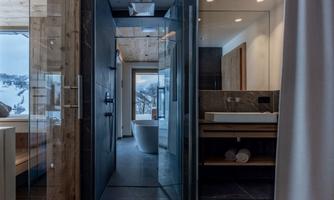 A modern bathroom with a glass shower and a bathtub. Large windows offer a view of the snowy landscape.