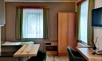 A modern room with a desk, chair, and a television. The large windows provide plenty of daylight, and the green decor brings a fresh atmosphere.
