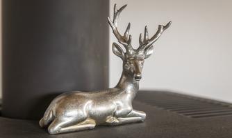 A silver deer figure lies on a dark background. In the background, a stove is visible.