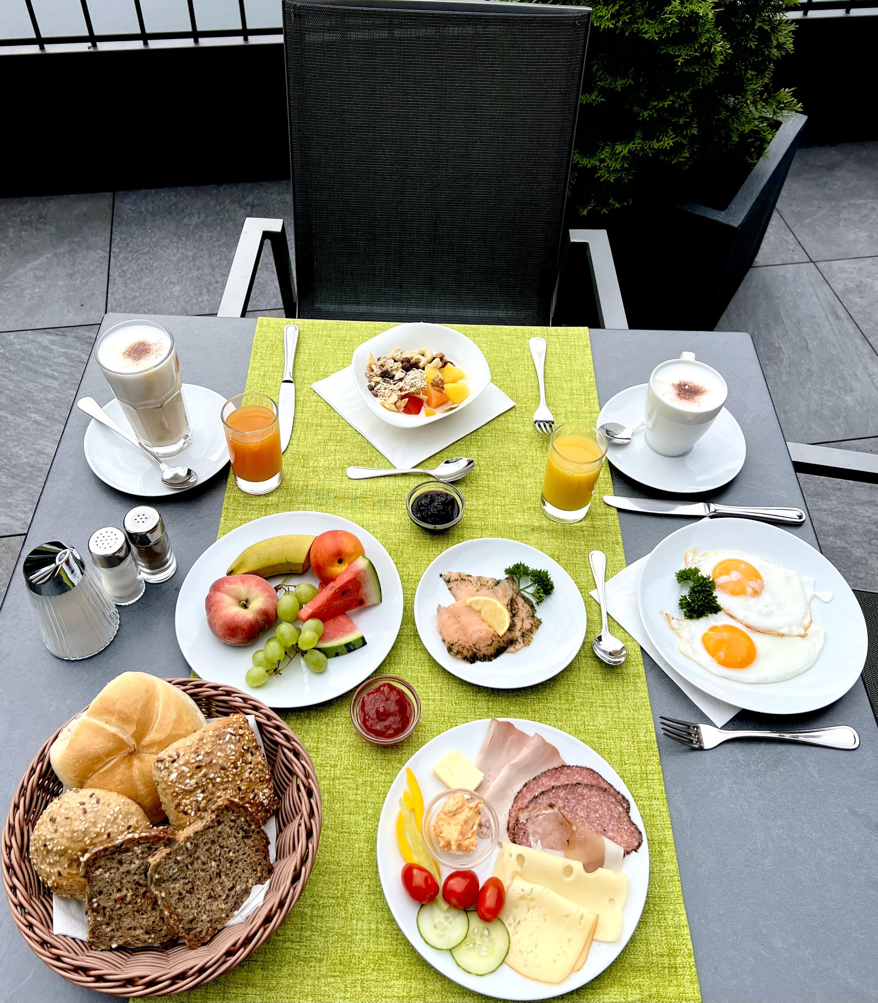 A varied breakfast on a table with different foods. There is fresh fruit, rolls, eggs, and drinks.