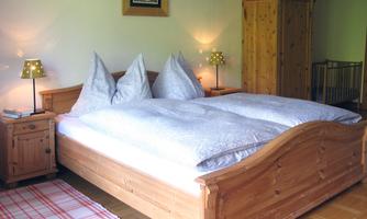 A cozy bedroom with a large bed and two pillows. There are wooden dressers and soft lighting that creates a warm atmosphere.